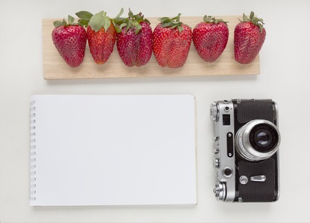 Notebook mock up for artwork with old camera, pen and red strawberries. Top view. Place for textの写真素材