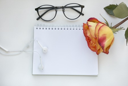 Notebook mock up for artwork with red and yellow rose, white headphones and gasses . Top view. Place for text. Fresh flowerの写真素材