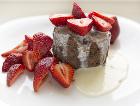 Delicious homemade chocolate cake with fresh red strawberries and cream sauce on white plateの写真素材
