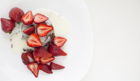 Delicious homemade chocolate cake with fresh red strawberries and cream sauce on white plateの写真素材