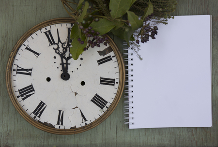 Old clock and blank notepad on the green wood background. New year background with plants and purple berries. Fresh leaves and purple berries. Vintage clocks.の写真素材