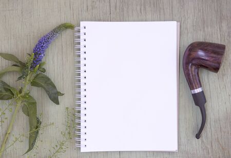 Mockup with blank notepad and smoking pipe. Blank sheet. A place for the presentation. Wild flowers on green painted wooden backgroundの写真素材