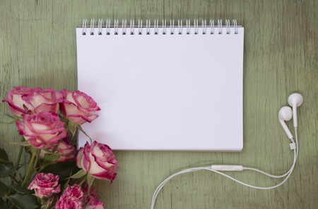 Blank notebook mock up for artwork with pink roses. Place for text. Fresh flowers ans white headphones.の写真素材