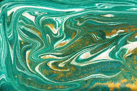 Liquid uneven green marbling pattern with golden glitter and glare of lightの写真素材