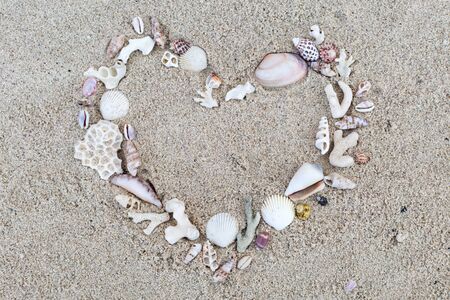Seashells and corals heart frame on sand background.
