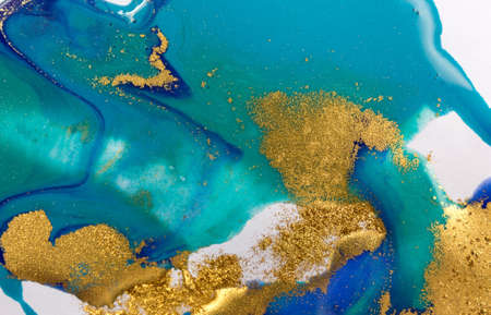 Gold and blue mixed inks splattered on white paper background.の写真素材