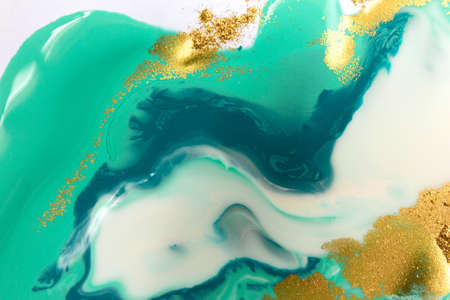 Piles of gold sequins on green and blue smudges of paint. Abstract pattern.
