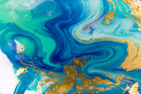 Gold and blue mixed inks splattered on white paper background.