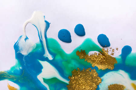 Gold and blue mixed inks splattered on white paper background.