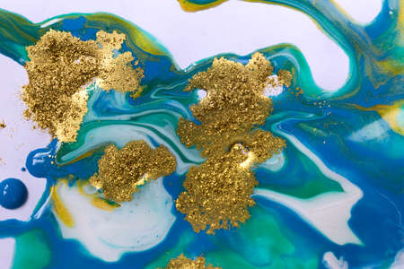 Gold and blue mixed inks splattered on white paper background