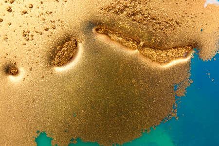 Piles of gold sequins on blue smudges of paint. Abstract pattern.