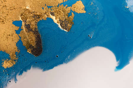 Piles of gold sequins on blue liquid ink background. Abstract pattern.の写真素材