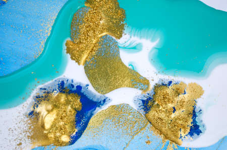 Close up gold scattered glitter on blue and white liquid backgroundの写真素材