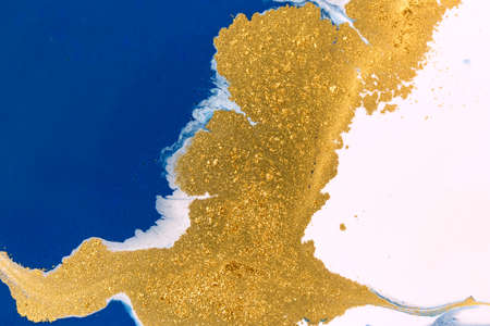 Cose up gold glitter on liquid blue and white paint background.の写真素材