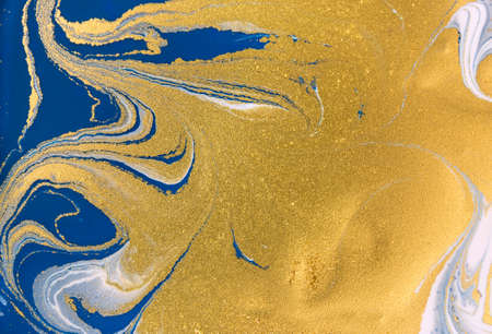 Cose up gold glitter on liquid blue and white paint background.の写真素材