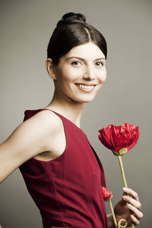 portrait of a beautiful woman with perfect skin and hair in a red dress with a flower on dark backgroundの写真素材