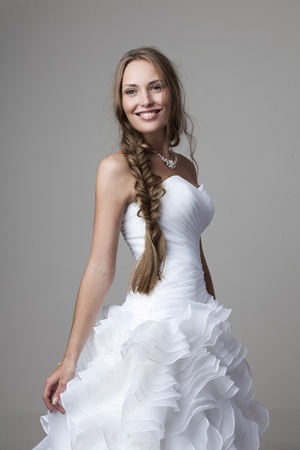beautiful smiling girl in a white wedding dress on a gray backgroundの写真素材