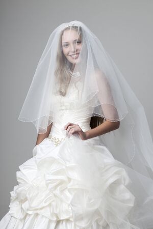 beautiful smiling girl in a white wedding dress with a veil on a gray backgroundの写真素材