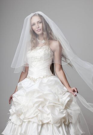 beautiful smiling girl in a white wedding dress with a veil on a gray backgroundの写真素材