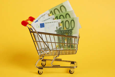 Mini shopping cart with euro banknotes on yellow backgroundの写真素材