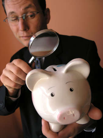   Businessman  looks to piggy bank through a magnifying glass (focus on piggy bank)          の写真素材