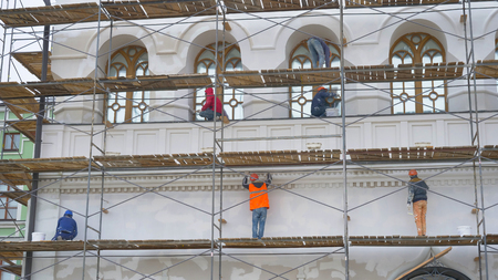 Painters standing on scaffolding paint the wall on construction site.のeditorial素材