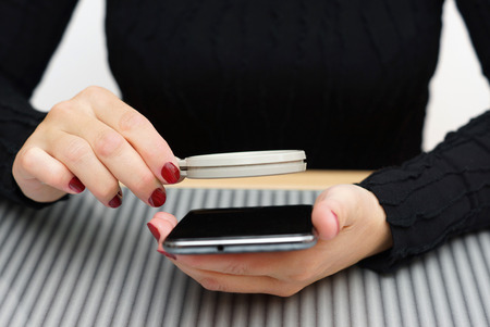 woman read small text on mobile phone with magnifying glassの写真素材