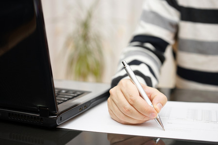 man is writing document or studying with a laptop beside at home