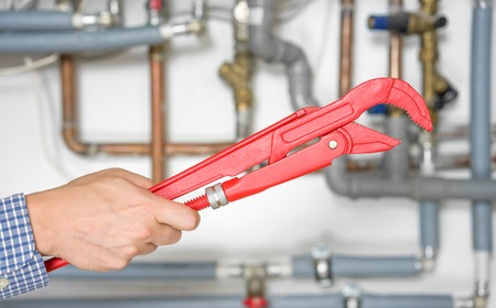 plumber holding pipe wrench with pipe system in background blurの写真素材