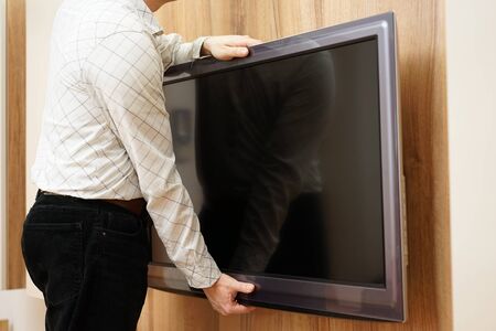 repairman gives television down from the wall in living roomの写真素材