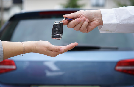 car dealer gives the customer the car keys with car in backgorund