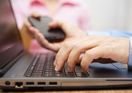 businessman is working on laptop computer and passing smart mobile phone to businesswomanの写真素材