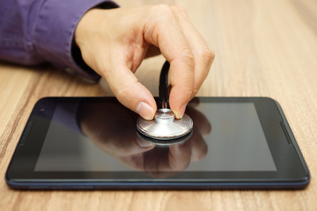 male  hand  is holding a stethoscope over tablet computer, repair service for tablet and laptopの写真素材