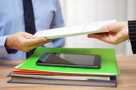 Associate passing a document to his colleague over stack of documentsの写真素材