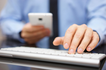 Businessman is using phablet while typing on computet keyboard, business and technology conceptの写真素材