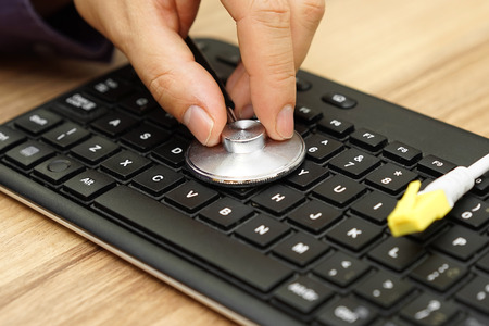 technician hand  is holding a stethoscope over computer keyboard and network cable, computer and internet maintenanceの写真素材