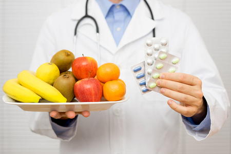 doctor holding healthy fruit  in one hand and pills in other hand,choosing between fruit or vitamin tabletsの写真素材