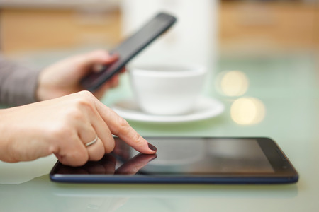 Woman is using tablet pc and smart phone in kitchen at the same timeの写真素材