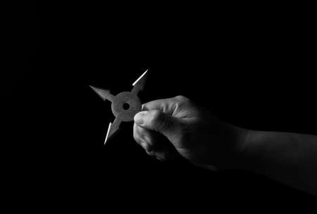 Closeup Hand Holding Ninja Star Shuriken Isolated on Black Background, Black and Whiteの写真素材