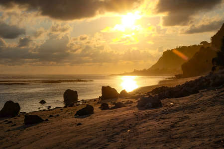 Evening sunset with rocks in the sand on the southern part of Bali with low tide and a tiny temple at the edge of the islandの写真素材