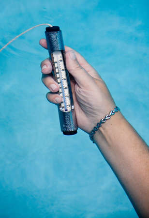 Female hand holding pool thermometer under waterの写真素材