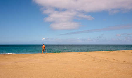 Rear view of fisherman on a wide sandy beachの写真素材
