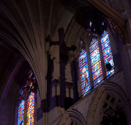 Light from stained glass windows falls on carved stonework in cathedral and casts shadow of crossの写真素材