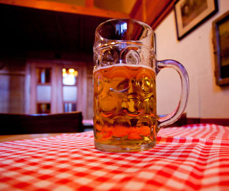 Close up of a liter glass of lager with a foamy head against a red and white tableclothの写真素材