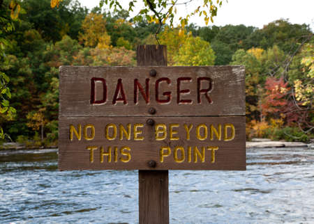 Wooden painted danger sign by rushing riverの写真素材