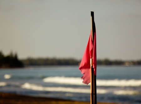 Sun setting lights up red flag signaling danger for swimming in surfの写真素材