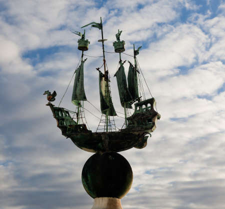 Small copper sailing ship set against a cloudy blue sky and showing its green colored copper sheenの写真素材