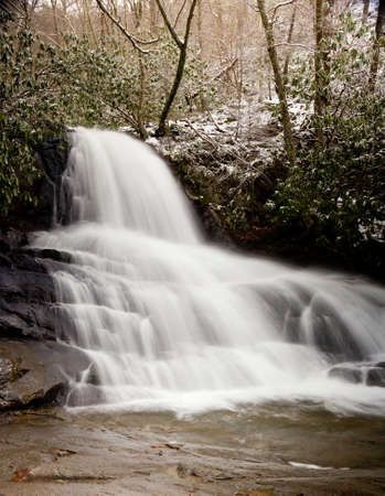 Snow covers the leaves and mountain as Laurel falls cascades over the mountainの写真素材