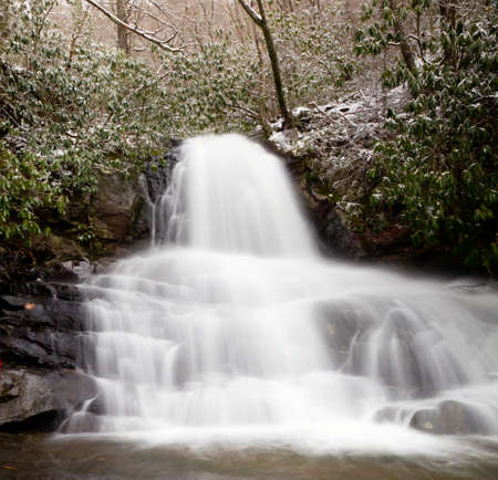Snow covers the leaves and mountain as Laurel falls cascades over the mountainの写真素材