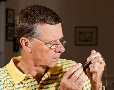 Senior repairing an old pocket watch with screwdriver and wearing very strong lens glasses to magnify the mechanismの写真素材